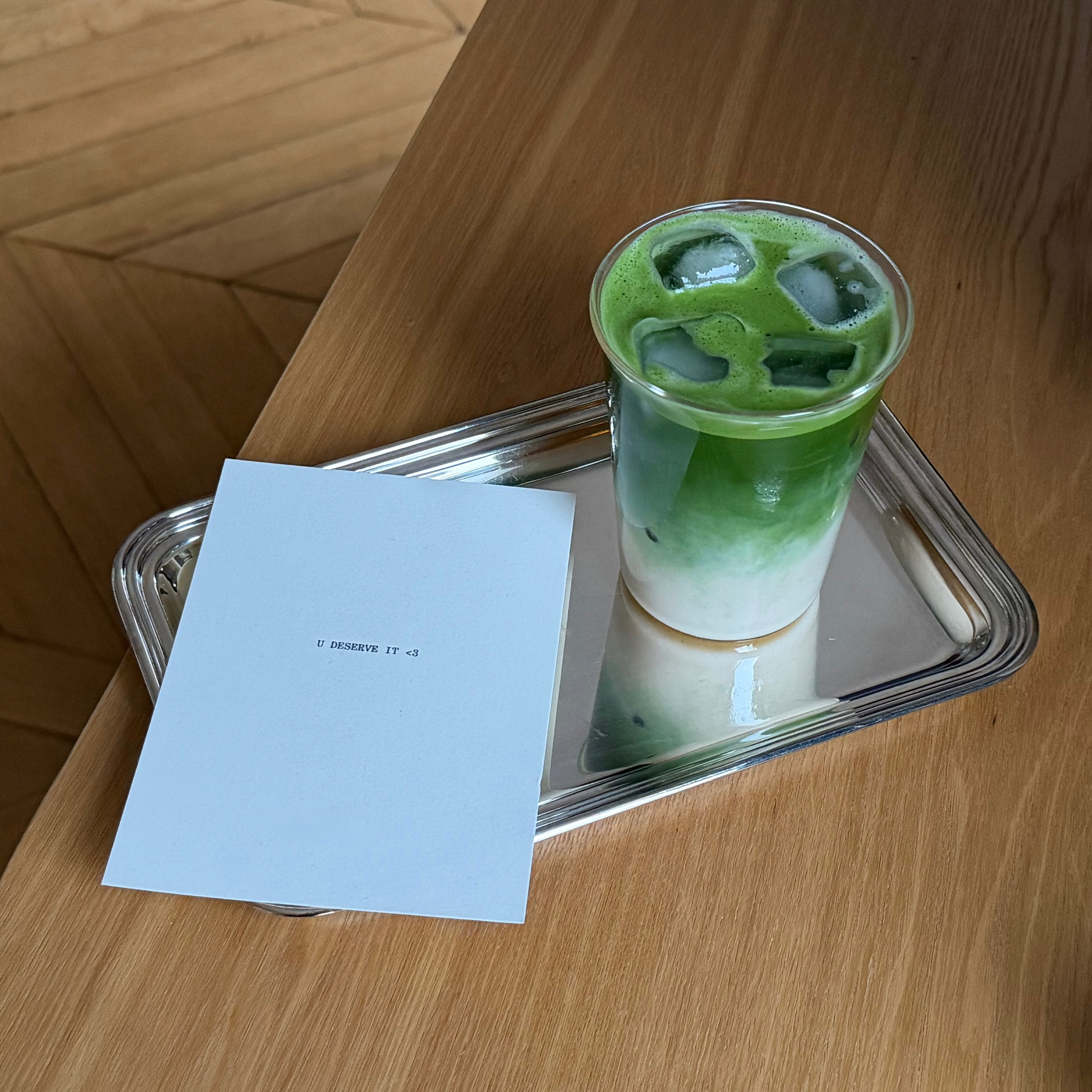 Green iced matcha in a glass on a tray with a piece of paper on a wooden surface